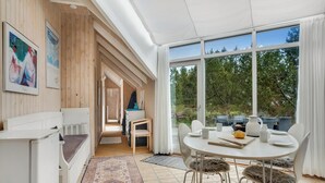 Quarto moderno com área de refeições, janelas amplas e vista para árvores.