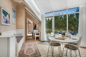 A modern room with a dining area, large windows, and a view of trees. - Family-friendly cottage with shared activities such as swimming pool, tennis. (Fjerritslev)