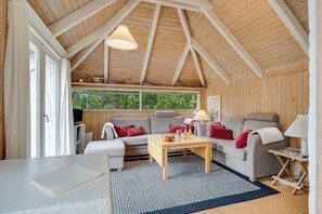 A cozy room with a wooden ceiling, a sofa, a table with drinks, and a view of greenery outside. - Family-friendly cottage with shared activities such as swimming pool, tennis. (Fjerritslev)