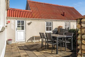 A house with a tiled patio, a dining table with chairs, and a stone wall. - Cozy holiday home near the water with space for 5 people (Snedsted)
