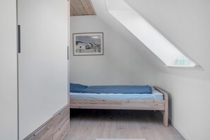 A small, single-bed room with a sloped ceiling and skylight, a framed picture on the wall, and a wooden floor. - Cozy holiday home near the water with space for 5 people (Snedsted)