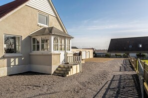 A building with a sloped roof, a covered porch, and a gravel driveway leading to a gated entrance.