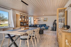 A modern living room with a dining area, wooden ceiling, and a view of the outdoors.
