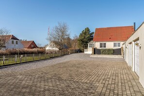 A paved driveway leading to a building with a red roof, a flagpole, and a hedge. - Cozy holiday home near the water with space for 5 people (Snedsted)