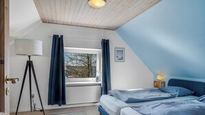 Ein Schlafzimmer mit zwei Betten, einem Fenster mit Vorhängen, einer Lampe und einer Heizung.