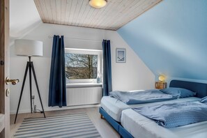 A bedroom with two beds, a window with curtains, a lamp, and a radiator.