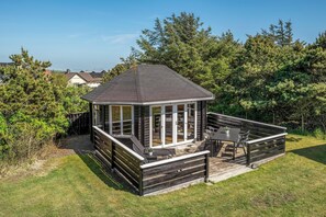 Eine Holzterrasse mit Glasveranda, Gartenmöbeln und Blick auf die umliegenden Bäume.