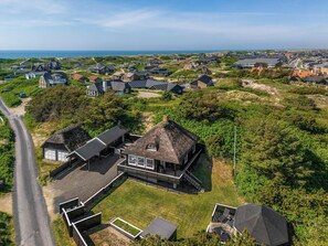 An aerial view of a coastal residential area with houses, a thatched-roof building, and a road. - Charming modernized holiday home in the heart of Søndervig (Ringkøbing)