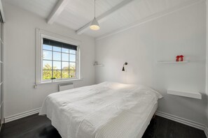 Ein Schlafzimmer mit einem Bett, einem Fenster, einem Heizkörper, einem Regal mit Dekoration und einer Pendelleuchte.