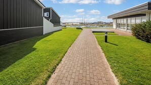 Un chemin menant à un bâtiment à l’architecture moderne, avec une pelouse et un ciel dégagé.