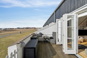 Eine überdachte Terrasse im Freien mit Grill, Sitzgelegenheiten und Blick auf die Landschaft.
