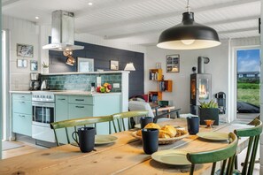 A modern kitchen with a dining area, featuring a wooden table, chairs, and a large pendant light. - Lovely holiday home with large terrace close to the North Sea in Klitmøller (Thisted)