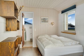Ein Schlafzimmer mit Bett, Holzregalen, einem Fenster und einer Tür zu einem anderen Raum.