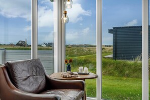 A leather chair, a small round table with candles, and a view of a grassy landscape through large windows. - Lovely holiday home with large terrace close to the North Sea in Klitmøller (Thisted)