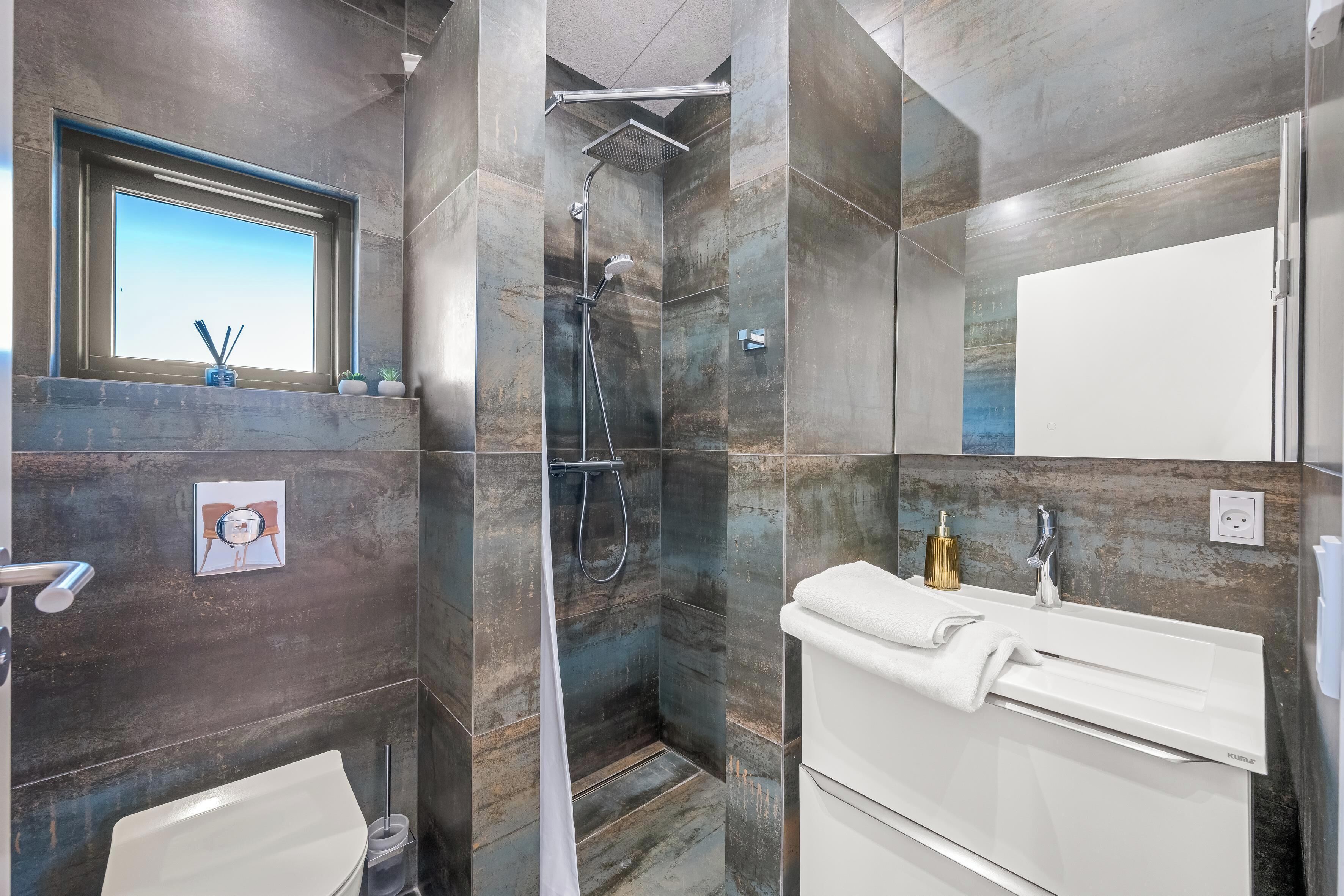 A modern bathroom with a shower, toilet, and sink, featuring a large window and a towel rack.