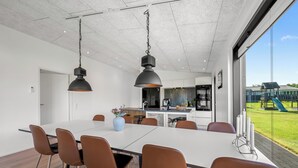 A modern dining area with a white table, brown chairs, and pendant lighting. - Lovely holiday home with mini golf course, sauna, wilderness bath and view of. (Vinderup)
