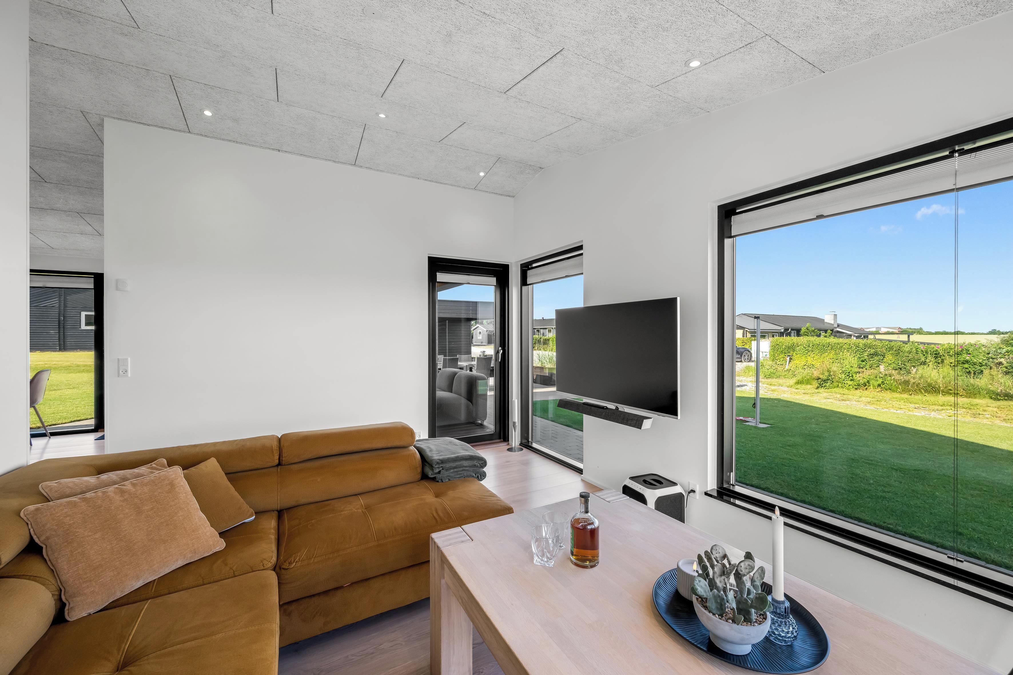 A modern living room with a sofa, a flat-screen TV, and a large window offering a view of a green lawn.