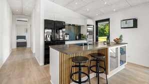 A modern kitchen with a central island, bar stools, and a view of the outdoors. - Lovely holiday home with mini golf course, sauna, wilderness bath and view of. (Vinderup)