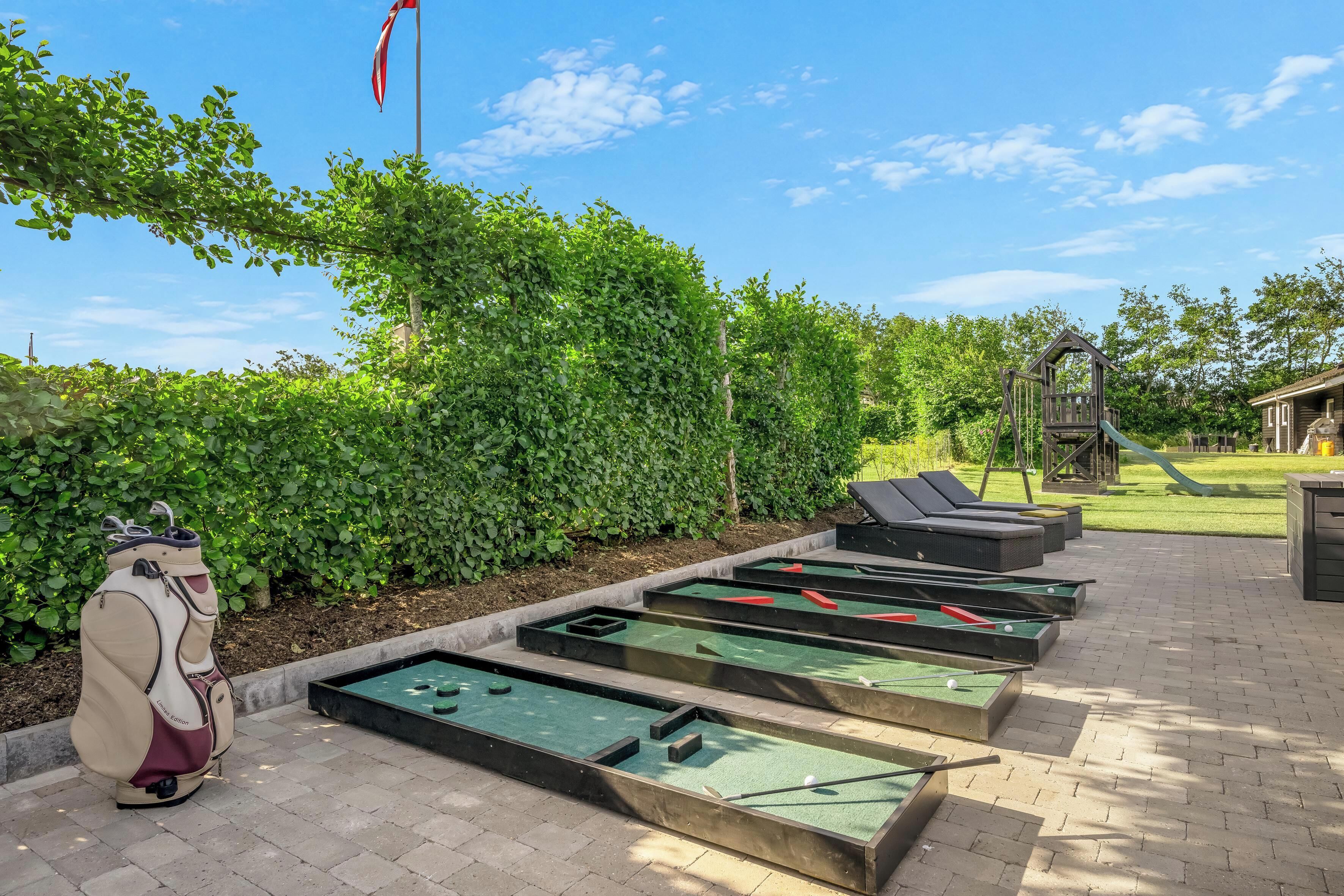 A shuffleboard court with multiple tables, a golf bag, and a wooden structure in a landscaped area.