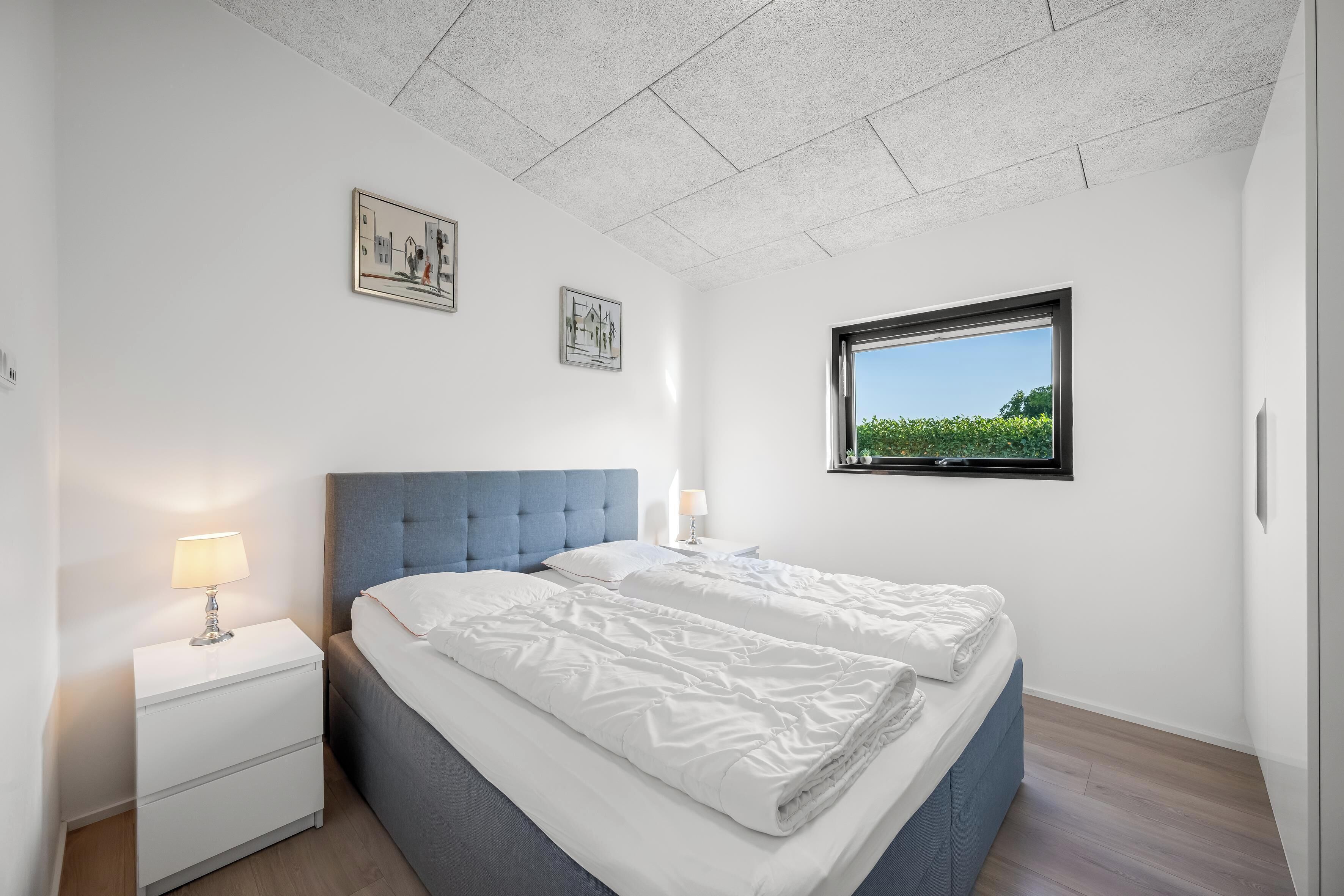 Ein Schlafzimmer mit Bett, Nachttisch, Fenster mit Aussicht und zwei Wandbildern.