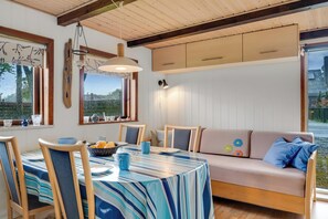 Un comedor acogedor con mantel a rayas, sillas de madera, un sofá con cojines y una lámpara colgante.