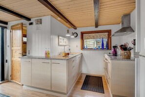 Una cocina con armarios de madera, estufa integrada, una ventana con botellas azules y un tapete negro.