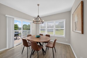 A dining area with a round table, six chairs, a chandelier, and large windows with blinds. - Cedar Lake 4br Home For 8 W/ Lake Views 4 Bedroom Home (Cedar Lake)