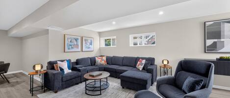 Un salon moderne avec un canapé d’angle, une table basse ronde et un fauteuil gris.