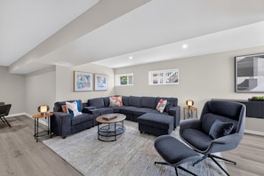 Ein modernes Wohnzimmer mit einer Eckcouch, einem runden Couchtisch und einem grauen Sessel.