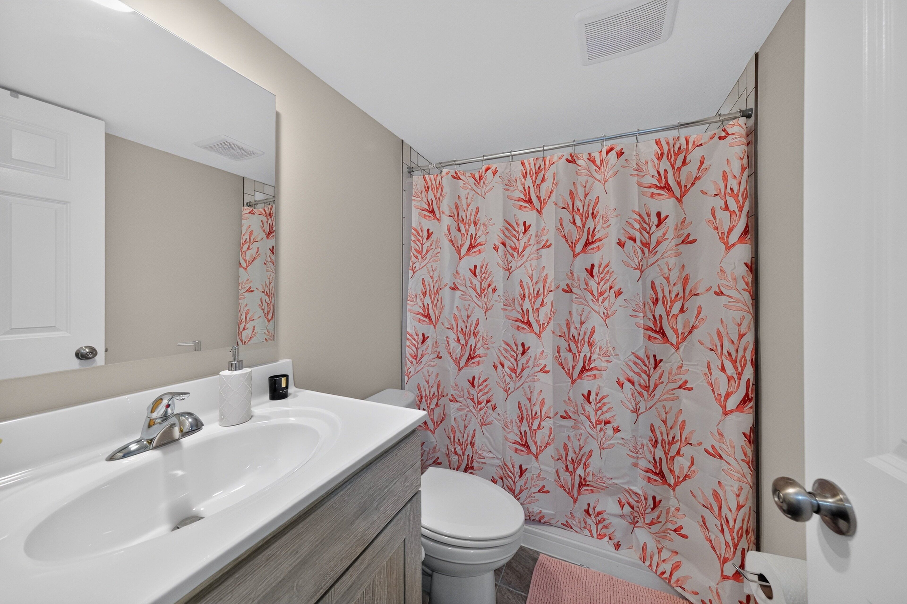 Une salle de bain avec un lavabo blanc, des toilettes et un rideau de douche orné d’un motif de feuilles.