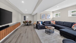 Ein modernes Wohnzimmer mit Flachbildfernseher, Ecksofa, Couchtisch und Essbereich mit Tisch und Stühlen.