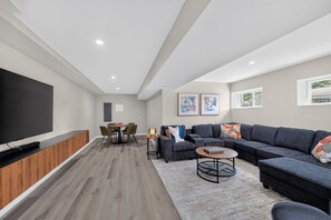 A modern living room with a flat-screen TV, a sectional sofa, a coffee table, and a dining area with a table and chairs. - Cedar Lake 4br Home For 8 W/ Lake Views 4 Bedroom Home (Cedar Lake)