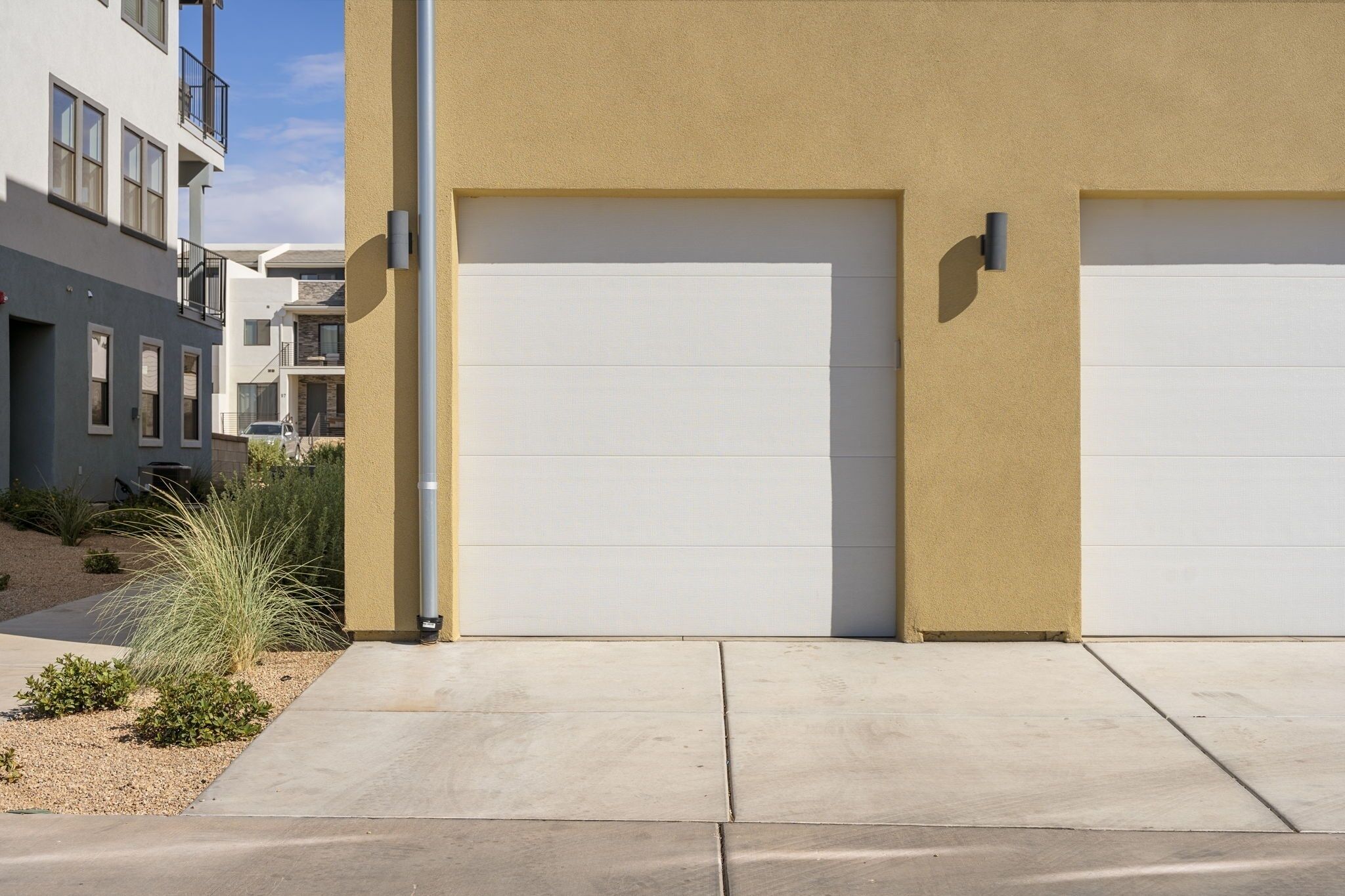A modern building with two garage doors, a concrete driveway, and a small landscaped area with plants.