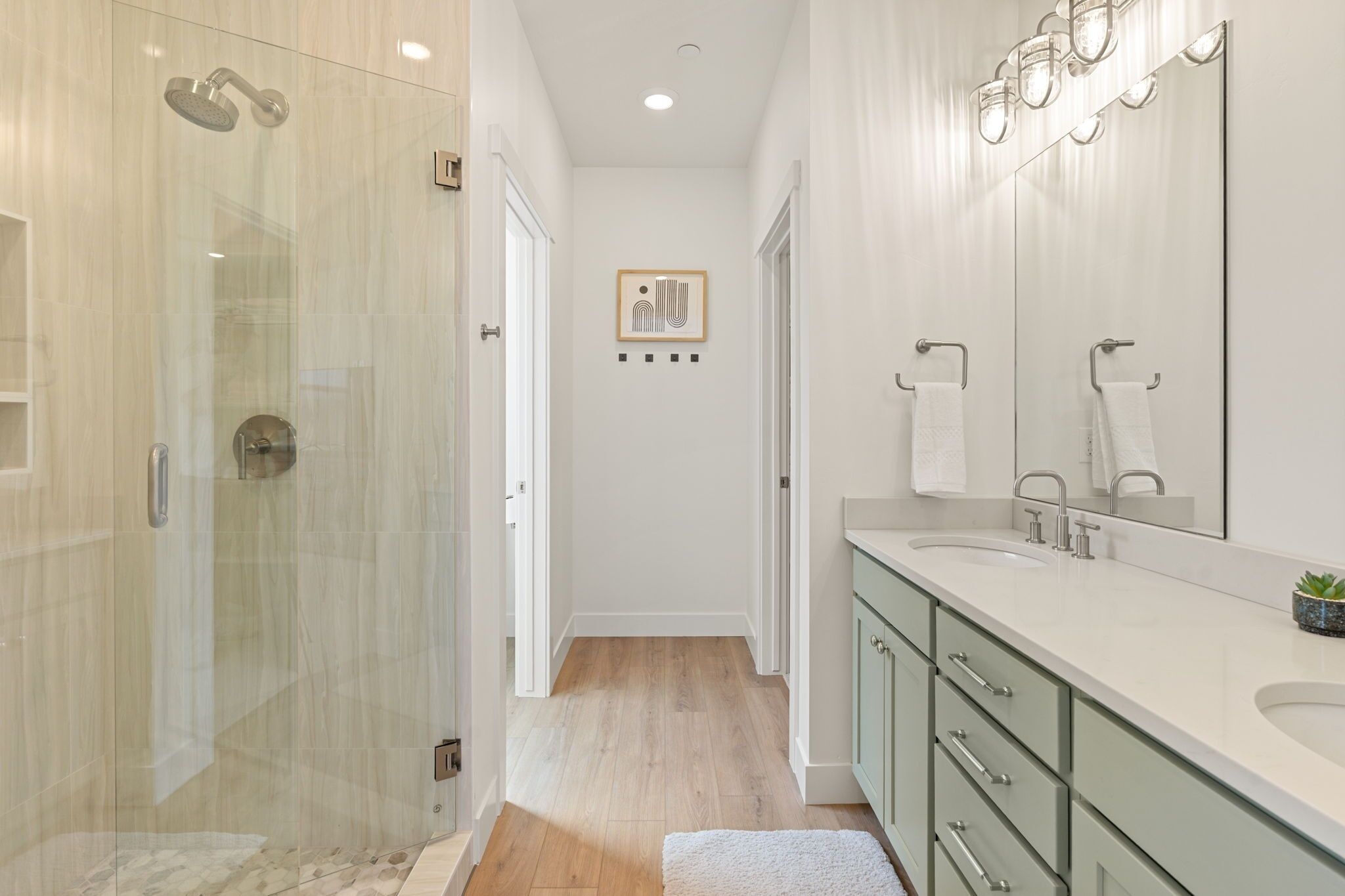A modern bathroom with a glass-enclosed shower, a large mirror, and a vanity with a sink.