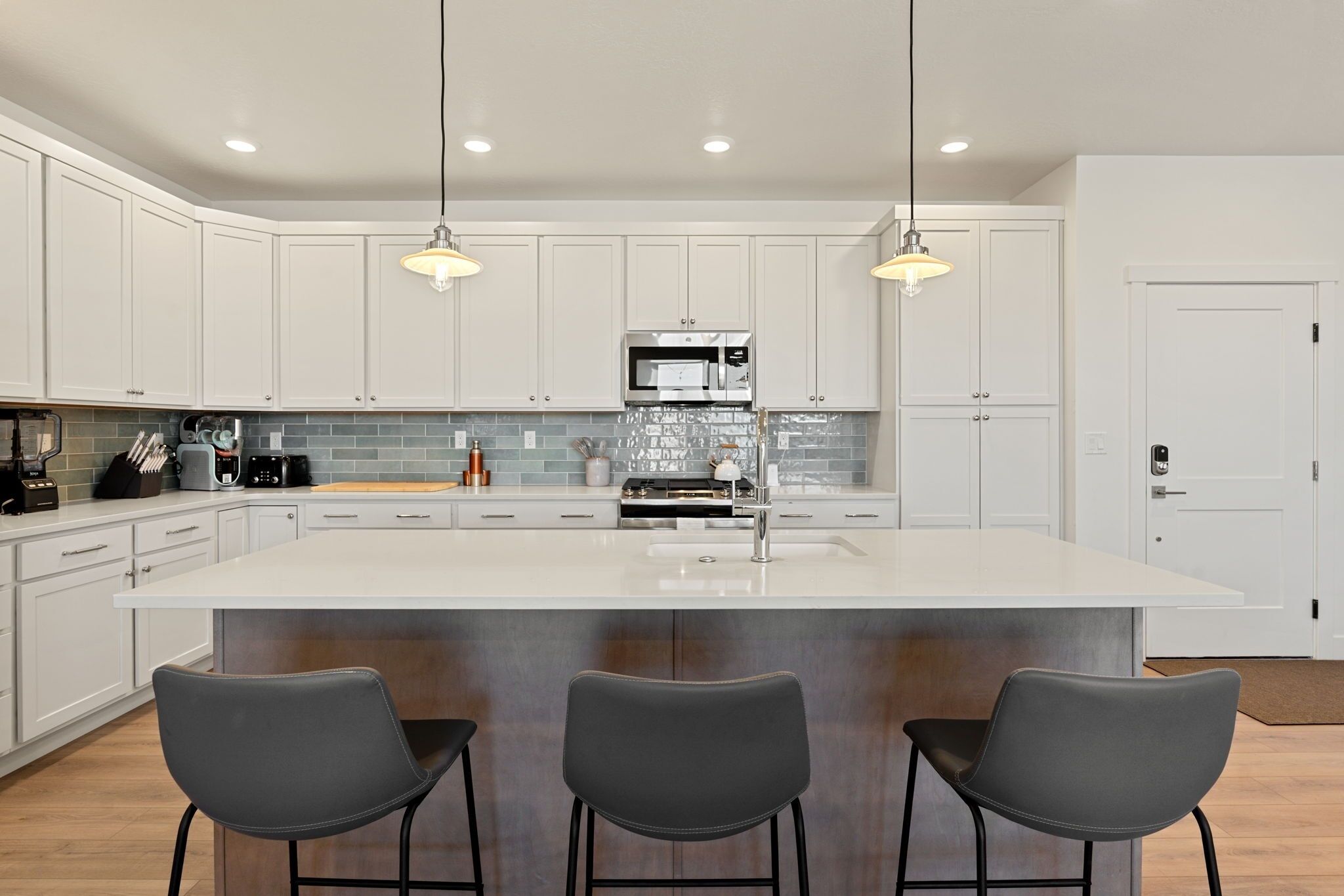 A modern kitchen with white cabinets, a large island, bar stools, and pendant lighting.