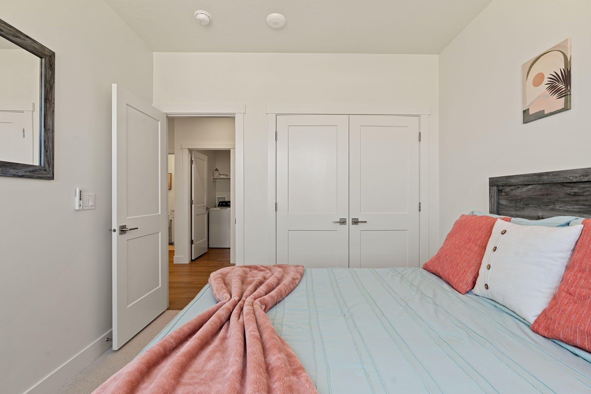 A bedroom with a bed, a wooden headboard, a pink blanket, and a white door.