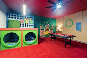 Ein Kinderspielbereich mit einer Billardkugel, einer grünen Spielanlage und einer Wand mit Mario-Motiven.