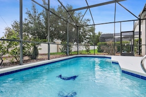 Ein Swimmingpool mit klarem, blauem Wasser, umgeben von einem Metallzaun und Glasschildern, mit Bäumen und einem Gebäude im Hintergrund.