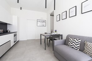 A modern kitchen with white cabinets, a dining table, and a gray sofa with patterned pillows. - GuestHost - Comfy TERRA Apartment near Cenisio MM5 (Milan)