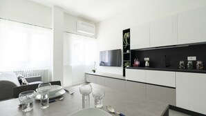 A modern kitchen with white cabinets, a black countertop, and a dining area with a table set for two. - GuestHost - Comfy TERRA Apartment near Cenisio MM5 (Milan)