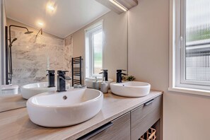 Ein modernes Badezimmer mit zwei großen weißen Waschbecken, einer Duschkabine aus Glas und einem Fenster für natürliches Licht.