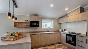 A modern kitchen with wooden cabinets, a built-in microwave, a gas stove, and a fruit basket on the counter. - Saron 2.0 Spa (Denbigh)