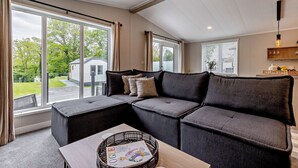 A modern living room with a sectional sofa, large windows, and a wooden table. - Saron 2.0 Spa (Denbigh)
