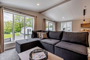 Ein modernes Wohnzimmer mit einer Eckcouch, großen Fenstern und einem Holztisch.