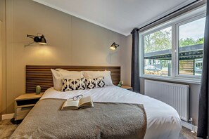 Ein modernes Schlafzimmer mit einem großen Bett, zwei Nachttischlampen, einem Nachttisch, einem Fenster mit Aussicht und einer Heizung.