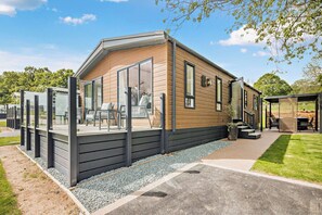 A modern single-story house with a large glass door entrance, a patio with outdoor furniture, and a well-maintained lawn. - Saron 2.0 Spa (Denbigh)