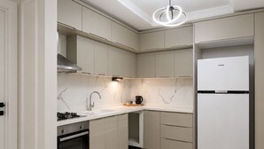Una cocina moderna con horno empotrado, campana extractora de acero inoxidable, refrigerador blanco y salpicadero de mármol.