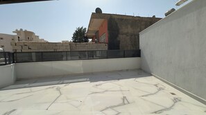 A rooftop terrace with a tiled floor, a low wall, and a view of surrounding buildings.