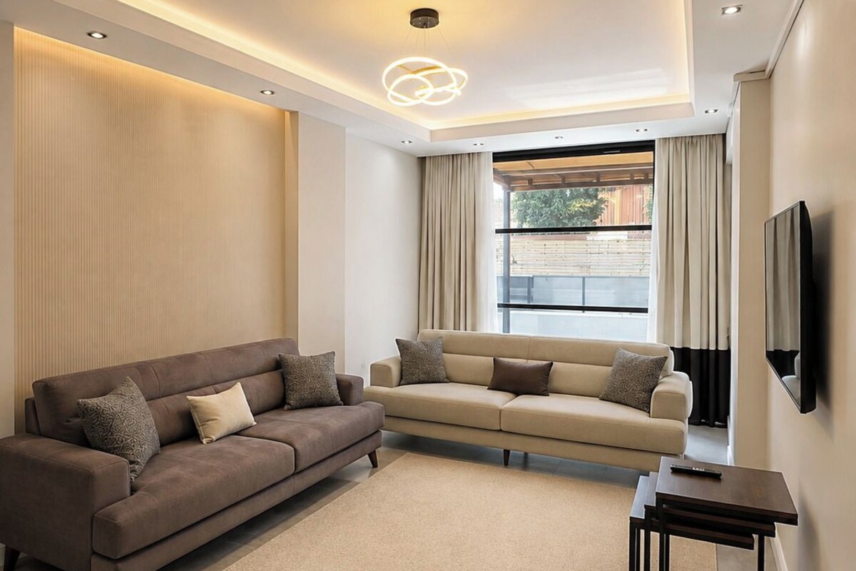 Un salon moderne avec un canapé d’angle, une table basse et un téléviseur à écran plat fixé au mur.