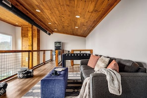 A cozy living area with a wooden ceiling, a sofa, a coffee table, and a foosball table. - Two cabins - Sleeps 24 - Views - Games - Outdoors (Sevierville)